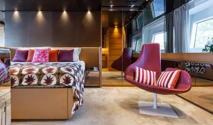 Takara One master cabin interior with beige sofa, red striped chairs, bed, and wood paneling