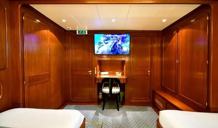 Tamarita cabin interior with twin beds, wood paneling, and a TV mounted opposite