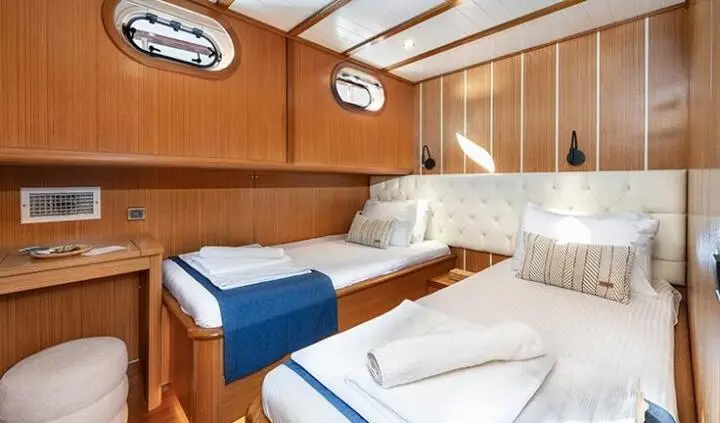 Twin cabin with two single beds, blue throw, wooden paneling and portholes