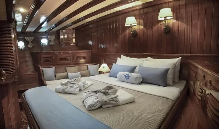 Master cabin with king bed, beige linens, wooden walls, and soft lighting