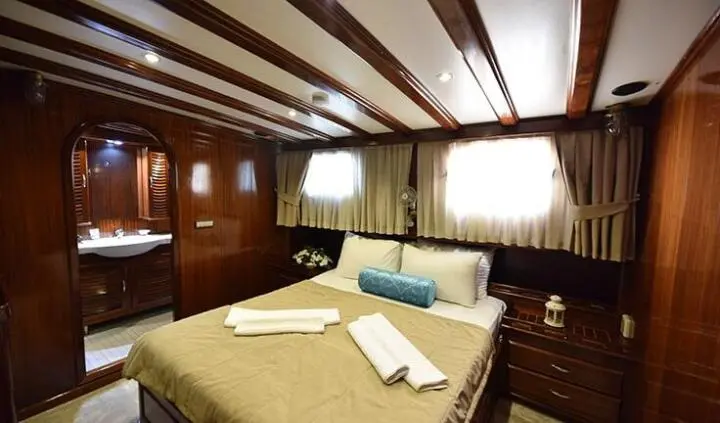 Cozy cabin interior on Kayhan Kaptan yacht with bed, wood panels, and porthole light
