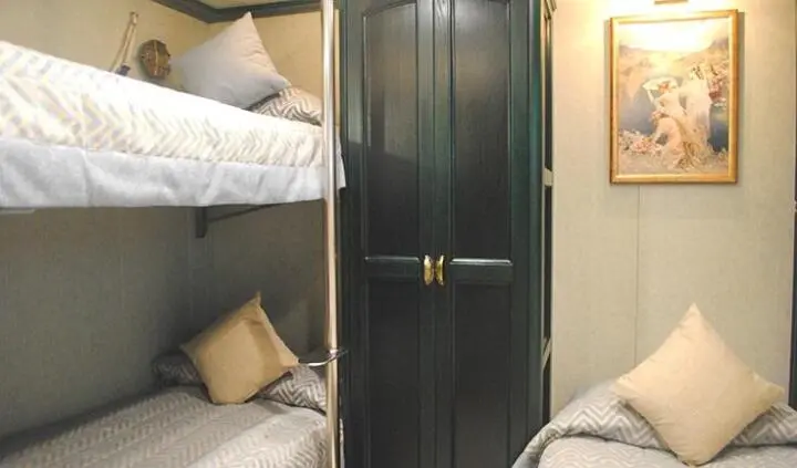 Two bunk beds with white bedding and a dark wooden wardrobe in a cabin