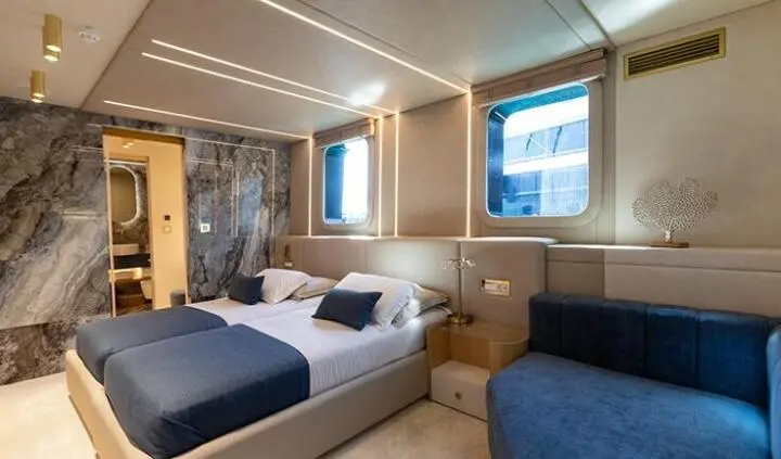 Scorpios yacht cabin with king bed, blue bedding, porthole window, and seating area