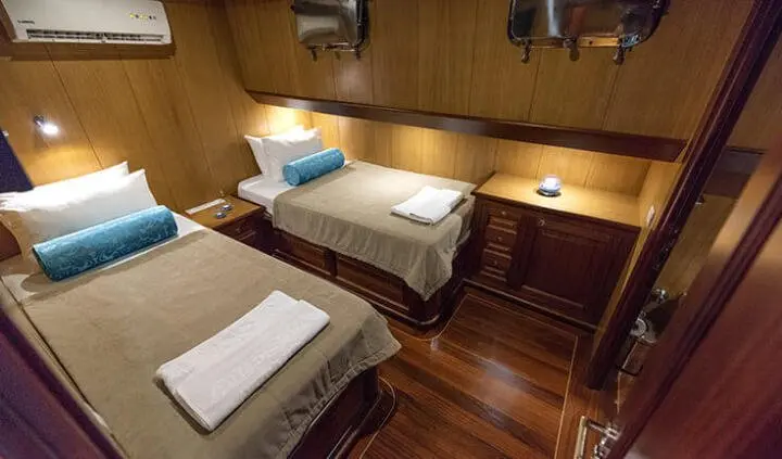 Twin cabin with two single beds, wooden paneling, and ensuite bathroom door