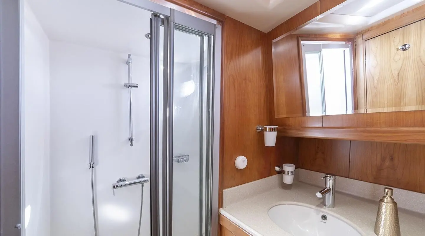 Queen Of Sea yacht interior: wooden walls, bathroom sink, mirror, and shower door