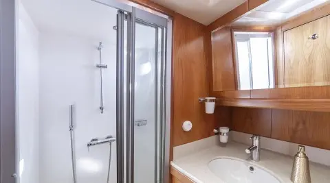 Queen Of Sea yacht interior: wooden walls, bathroom sink, mirror, and shower door