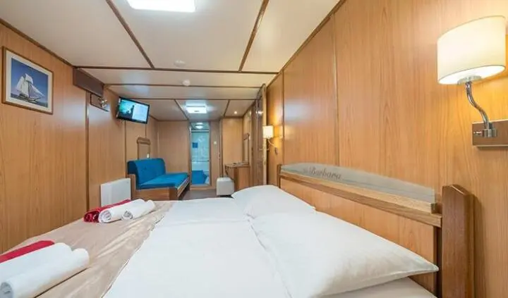View of a yacht cabin interior with two single beds, wood walls, and seating area
