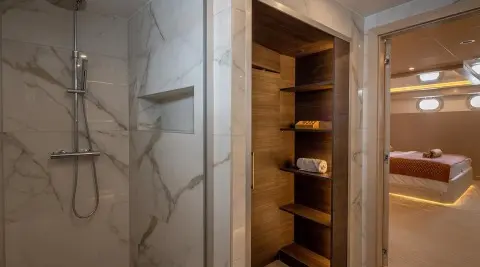 Open wooden built-in closet with shelves and a marble wall behind it on a yacht interior