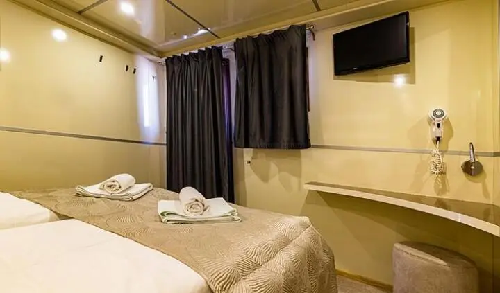 Two single beds with beige bedding in a compact cabin, towels folded on each bed