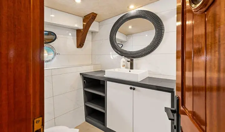 Esma Sultan cabin bathroom with circular mirror, white cabinets, and a tiled wall.
