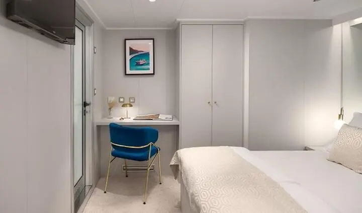 Master cabin with king bed, ensuite, nightstand, and blue chair beside desk