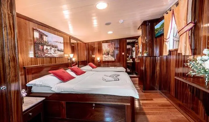 Master cabin with king bed, white linens, wood cabinetry, and ensuite bathroom visible