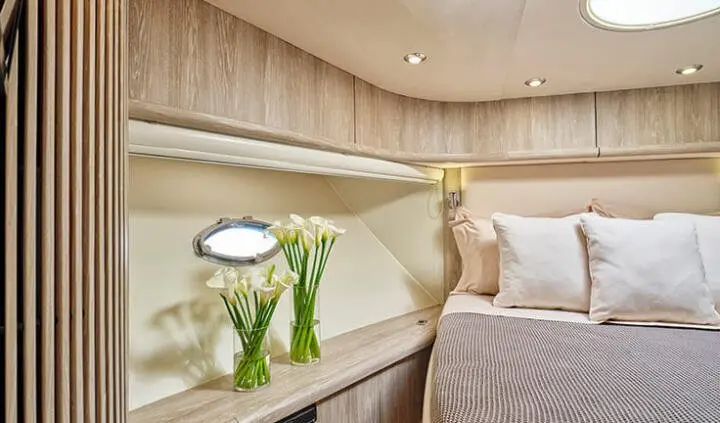 Master cabin with king bed, porthole window, and cream decor on yacht
