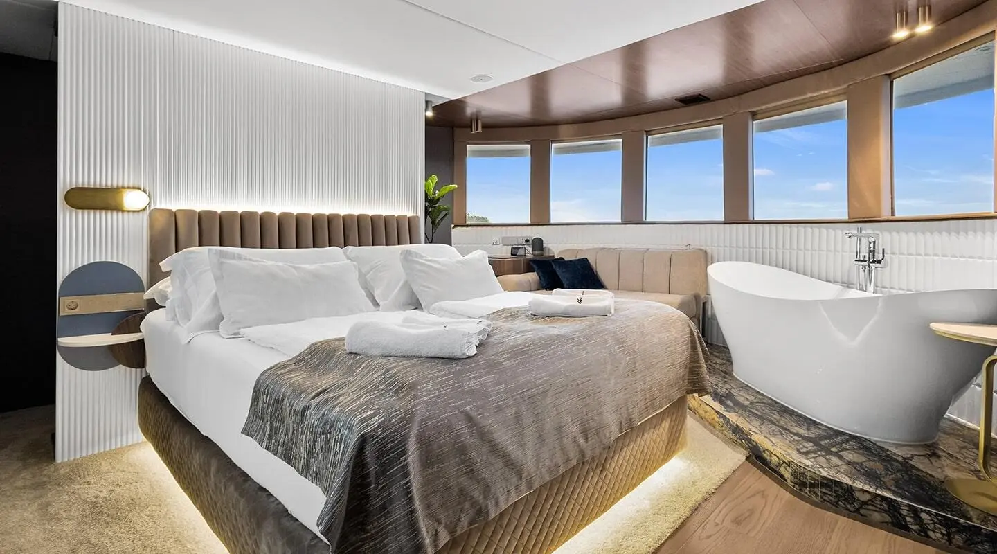 Bella luxury yacht bedroom with large bed, sunkown lighting, and windowed deck view