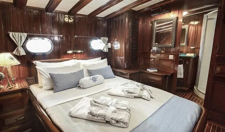 Master cabin with king bed, two pillows, and wooden walls aboard yacht Entre Cielos