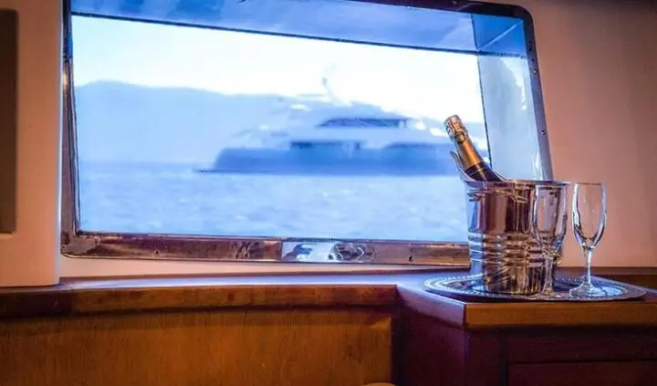 View from a yacht cabin with a large porthole showing the calm sea and another vessel in distance