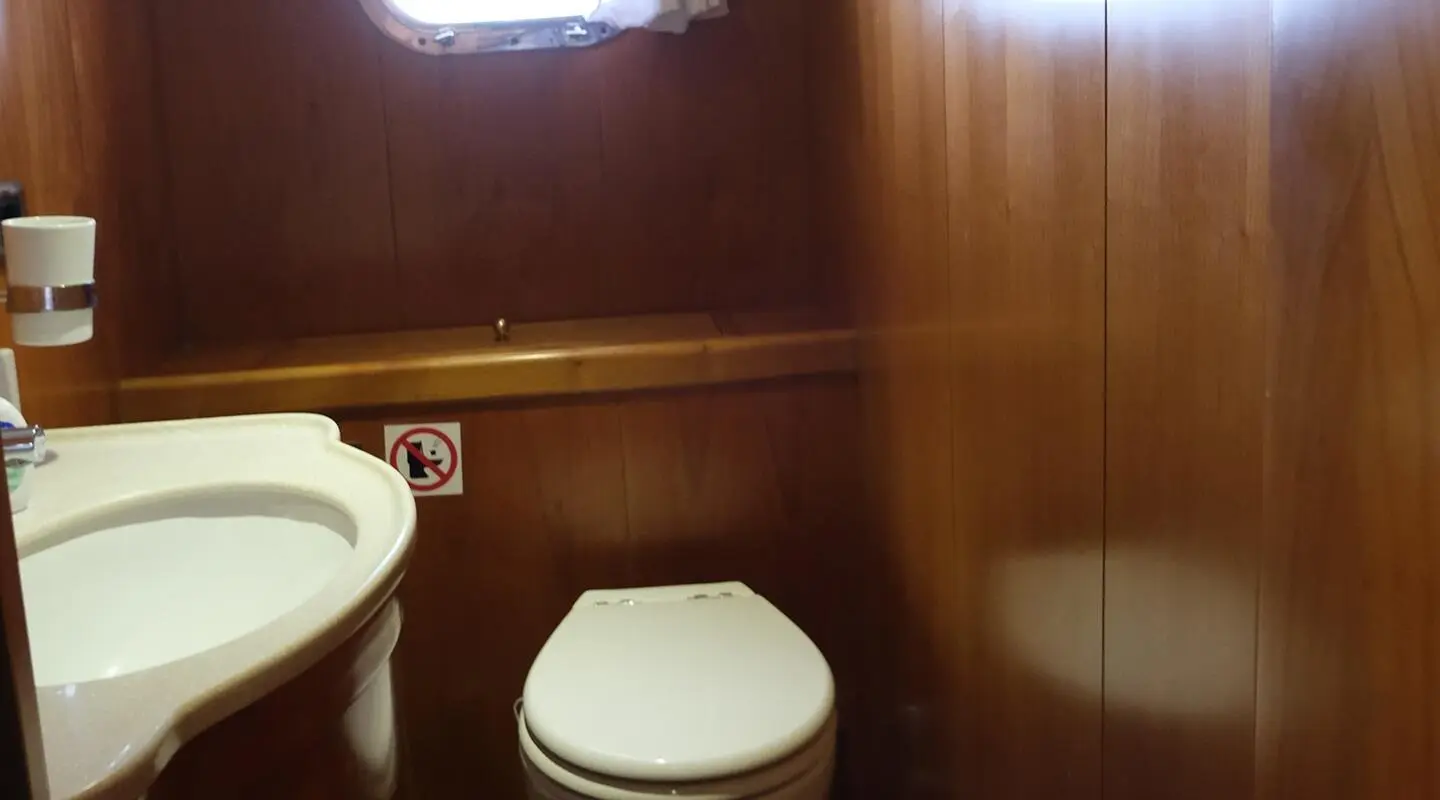 Wood-paneled yacht bathroom with white toilet and compact sink area