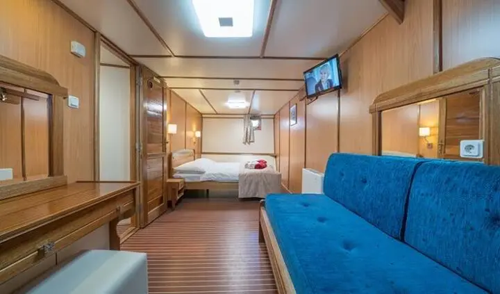 Master cabin with king bed, ensuite door, wood paneling and blue sofa