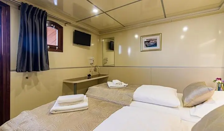 Melody yacht cabin with two single beds, beige walls, and mounted TV