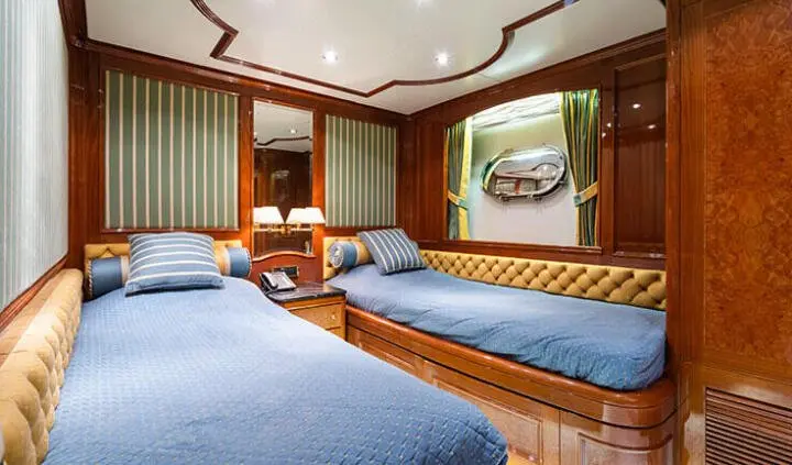 Twin cabin on Amadea yacht with two single beds, wood paneling, blue bedding, and porthole window