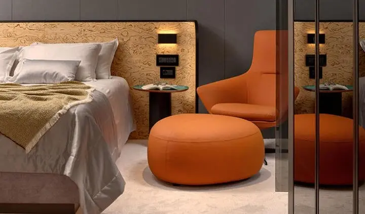 Master cabin with king bed, beige linens, wood headboard, orange ottoman and chair