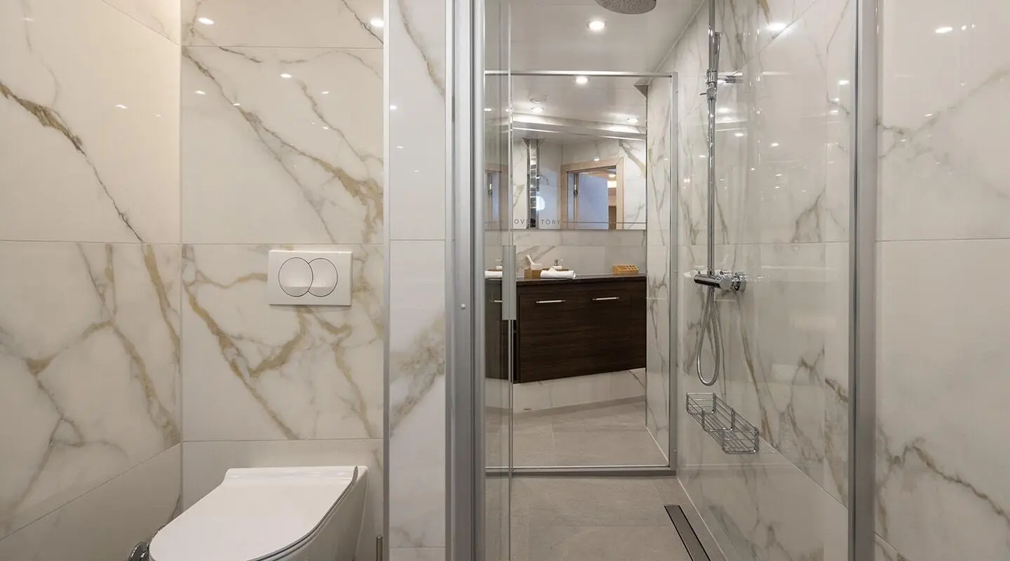 Love Story yacht bathroom with marble walls, glass shower, and wooden vanity