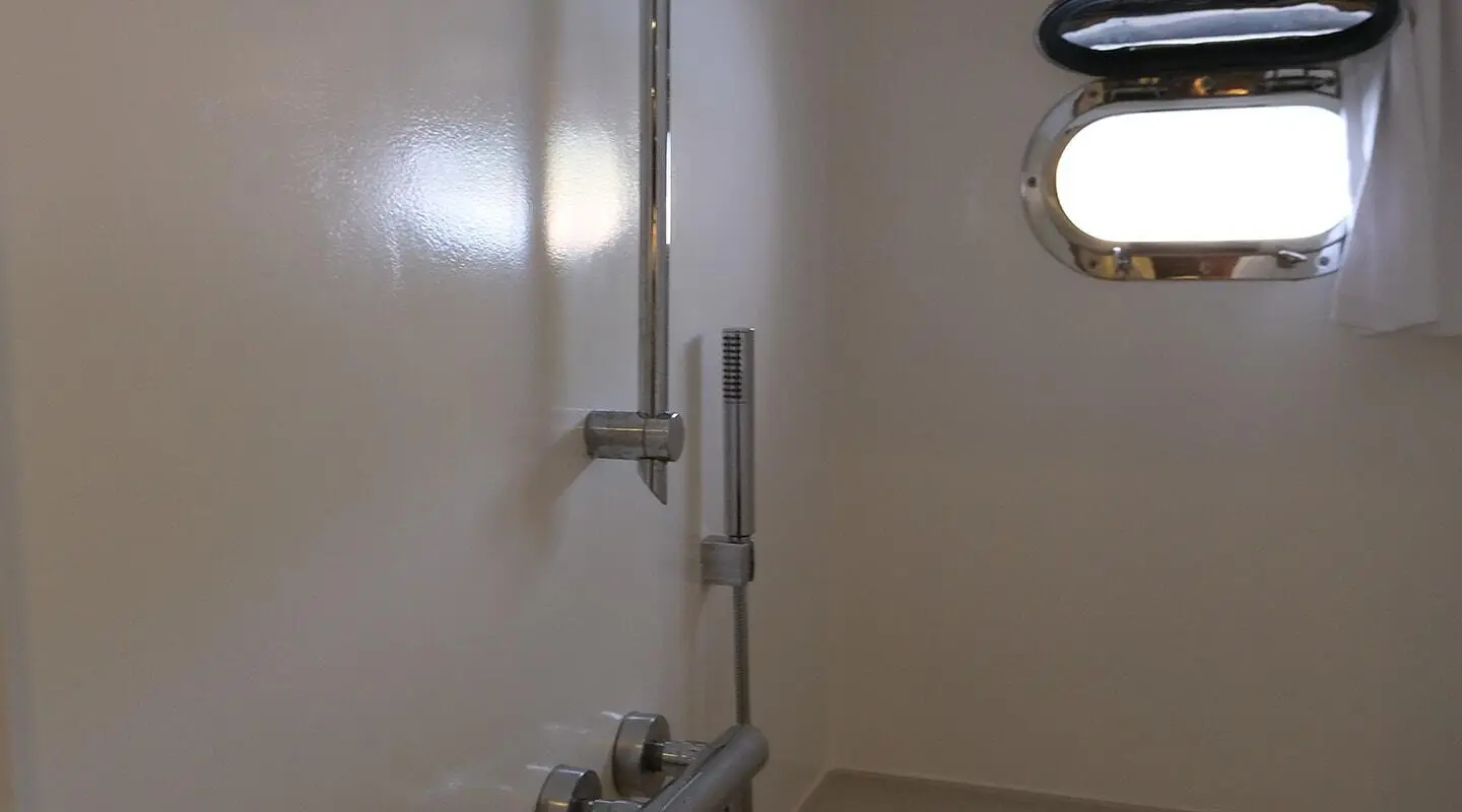 Shower area aboard Queen Of Sea with wall pipe, handheld shower, and window light