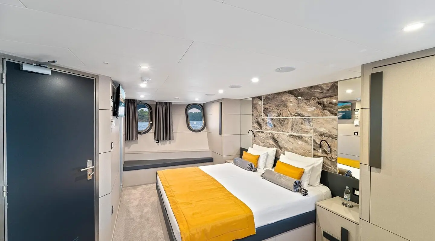 Luxurious bedroom on Freedom yacht with two beds, stone wall, and yellow throws