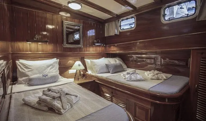 Master cabin with two single beds pushed together, wood paneling, porthole window, and bedside shelves