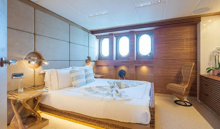 Serenity cabin bed with white linens, porthole windows, wooden walls, and ensuite area