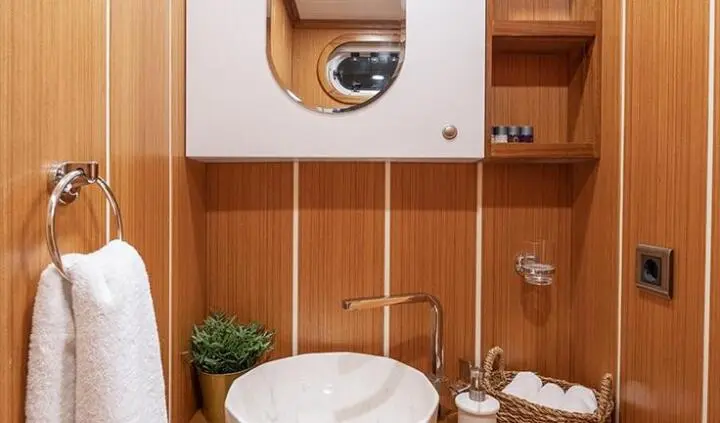 Yacht cabin sink with round mirror, wooden panels, and towel on rack