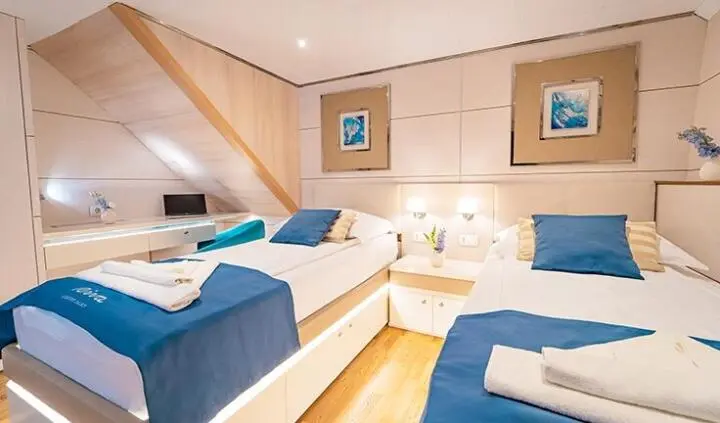Twin cabin on a yacht with blue and white beds and built-in wooden storage