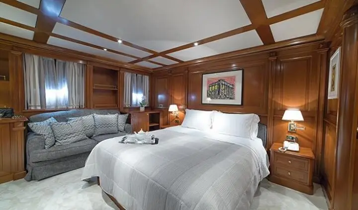 Aquila yacht cabin with a plush bed, wooden paneling, and a gray sofa