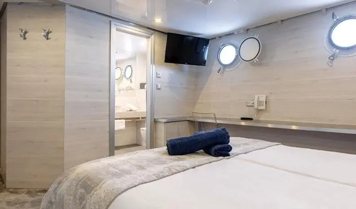 Yacht cabin with king bed, seating, portholes, and ensuite area visible