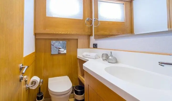 Small yacht cabin with wooden walls, sink, mirror, and toilet visible
