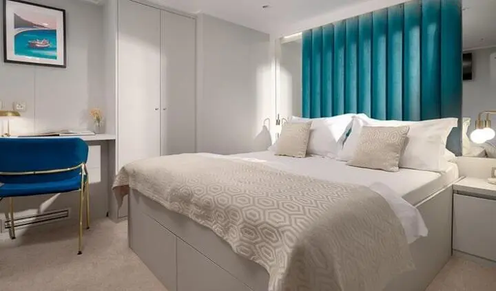 Master cabin with two beds, neutral tones, and teal window blind view