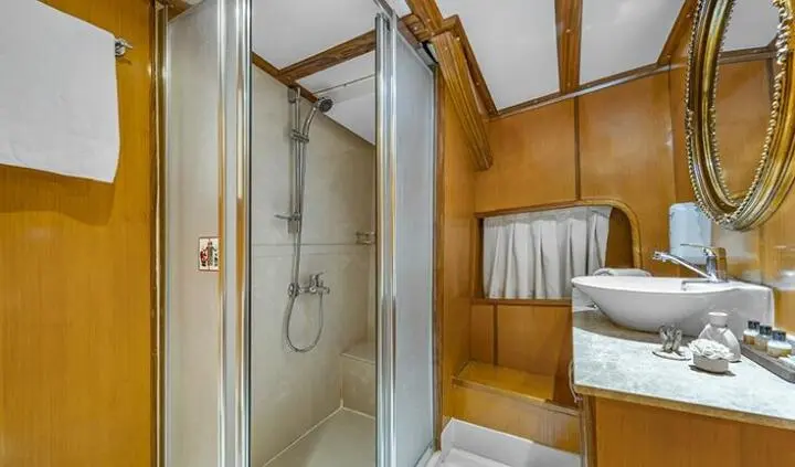 Yacht guest cabin ensuite with glass shower door, wooden walls and sink