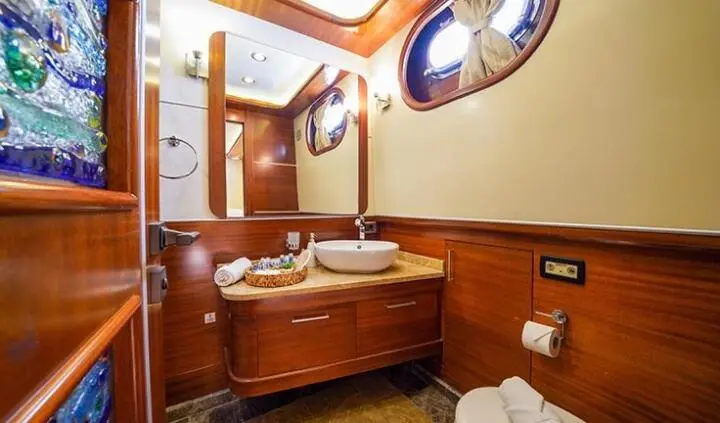 Master cabin with wooden vanity, double sink, round porthole window, beige walls