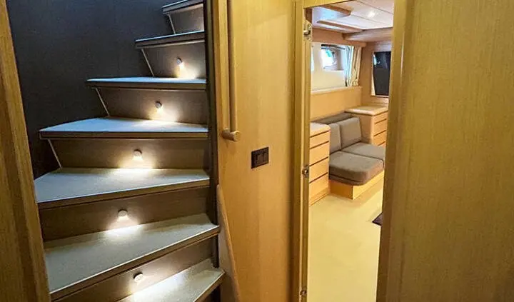 View of a yacht cabin with stairs on left and a doorway leading to a small bed area