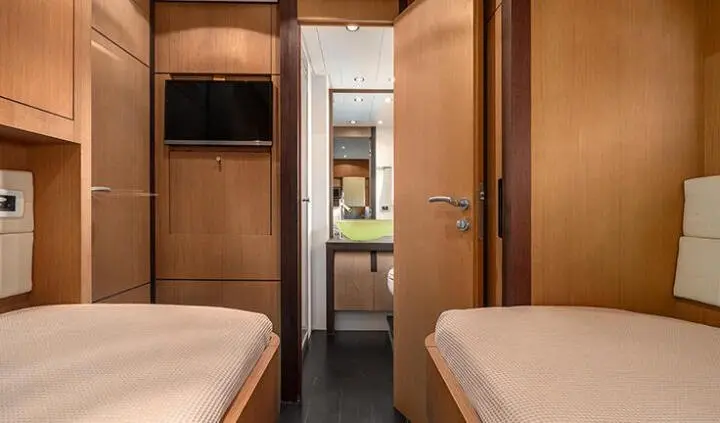 Twin cabin interior on a yacht with wood panels, beds, and doorway.