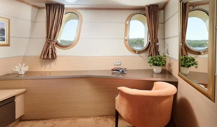 Queen Eleganza cabin bed with beige walls, porthole windows, and a brown chair
