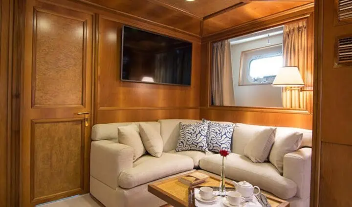 Cozy yacht cabin with beige sofa, cushions, wood paneling, and TV