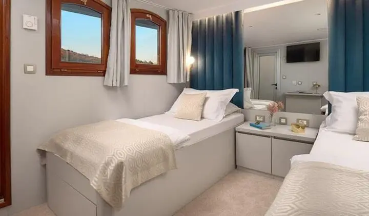 Two beds in a bright cabin on Bellezza yacht, beige linens and blue curtains
