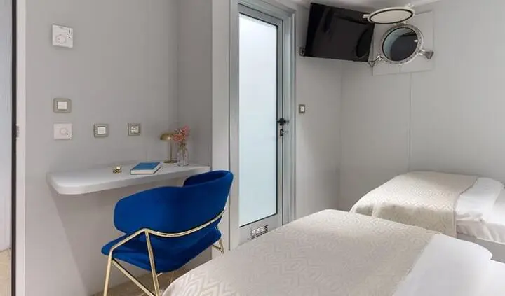 Two twin beds in a cabin with a desk and a blue chair, minimal white walls