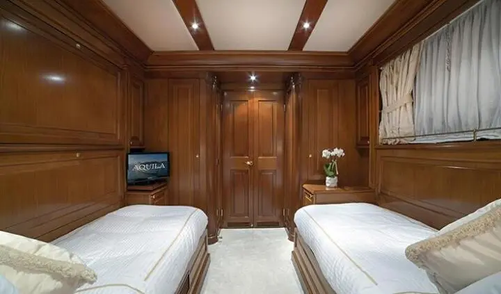 Aquila yacht cabin interior with twin beds and wooden panels, warm lighting