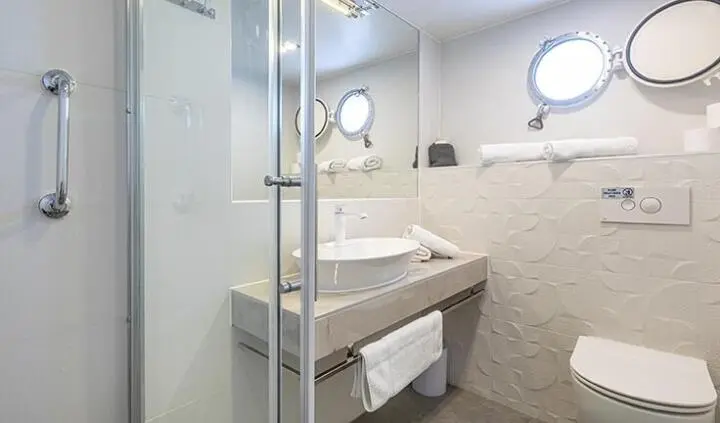 Yacht cabin with bed, ensuite bathroom, circular porthole windows, neutral decor