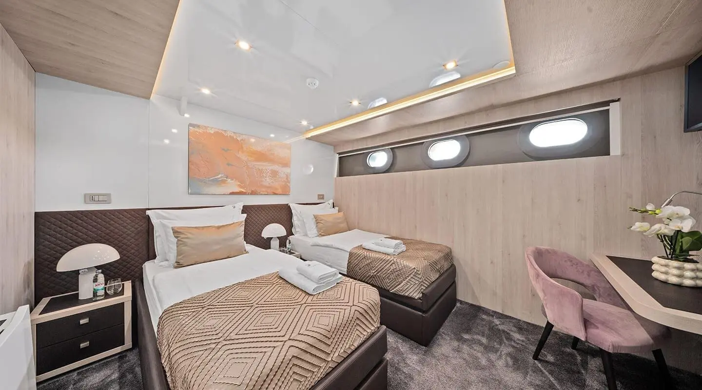 Interior of Dalmatino yacht with beige bedding, brown sofa, and overhead lighting