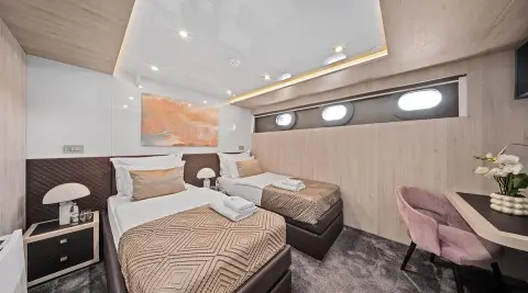 Interior of Dalmatino yacht with beige bedding, brown sofa, and overhead lighting