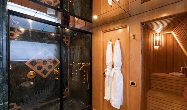 Luxurious yacht cabin with wooden panels, robes on door, and glass shower enclosure