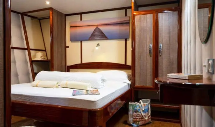 Master cabin with king bed, white linens, wood cabinetry, ensuite doorway